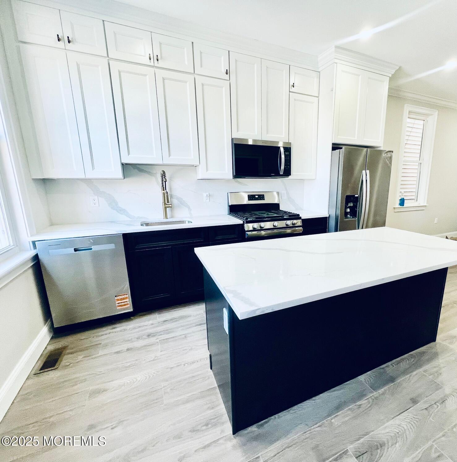 a kitchen with stainless steel appliances a sink a stove a refrigerator a center island and cabinets