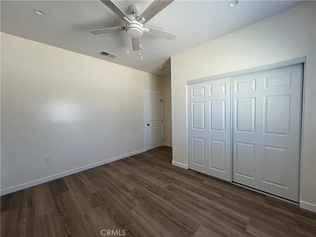 an empty room with wooden floor closet and fan