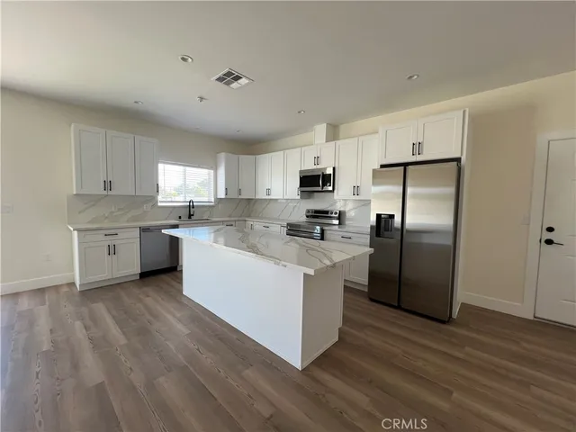 a kitchen with stainless steel appliances granite countertop a stove a sink dishwasher a refrigerator and white cabinets with wooden floor