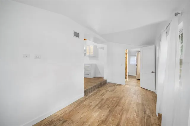 a view of an empty room with wooden floor and a kitchen