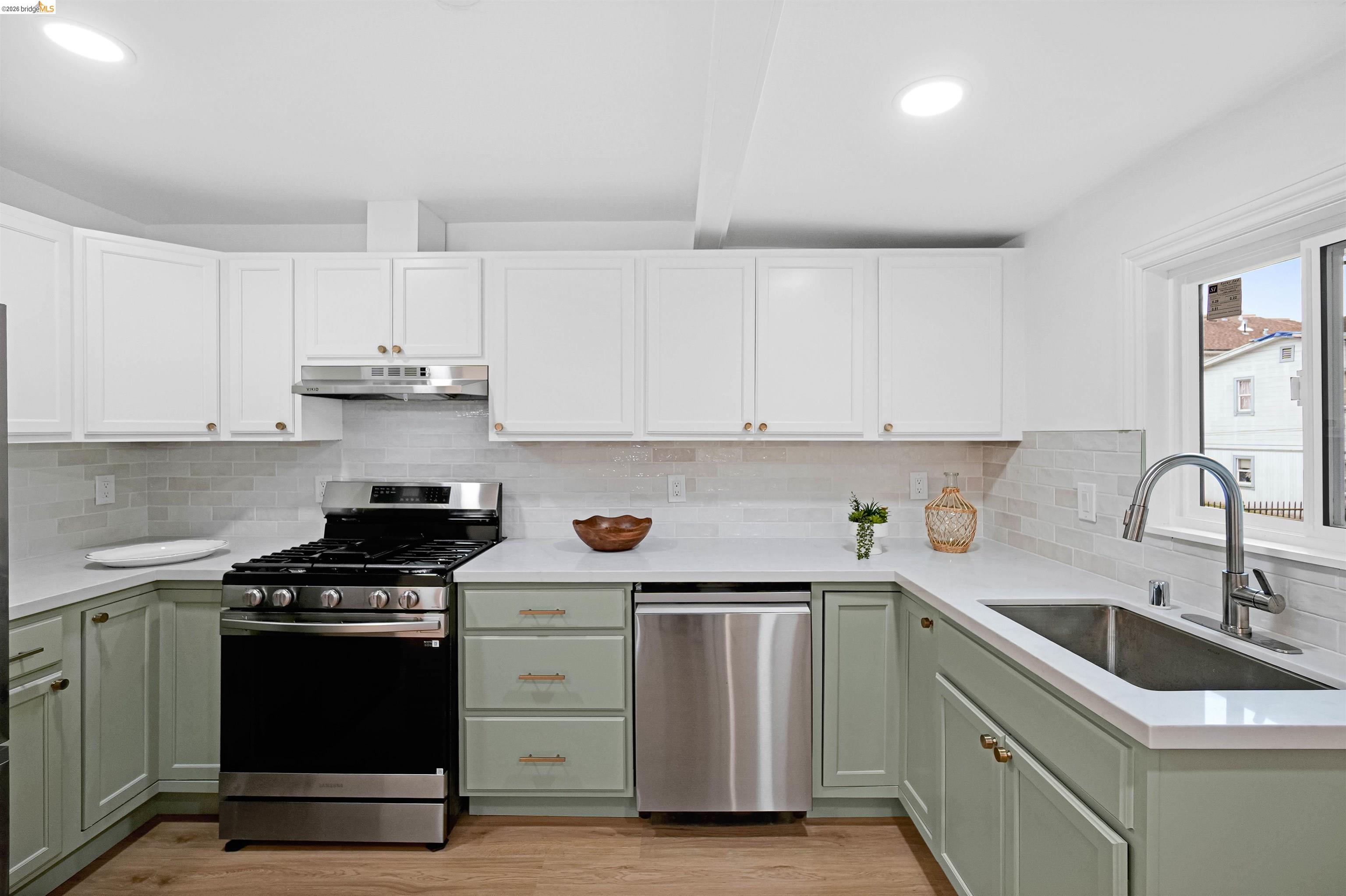 1812 Woolsey Street Berkeley, CA 94703 - Photo 11 of 48 Modern kitchen featuring two-tone cabinetry with white upper and light green lower cabinets, stainless steel appliances, white countertops, and a subway tile backsplash