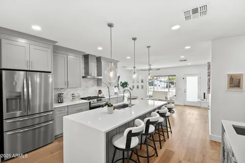 a kitchen with stainless steel appliances kitchen island granite countertop a sink a stove a refrigerator and island with wooden floor