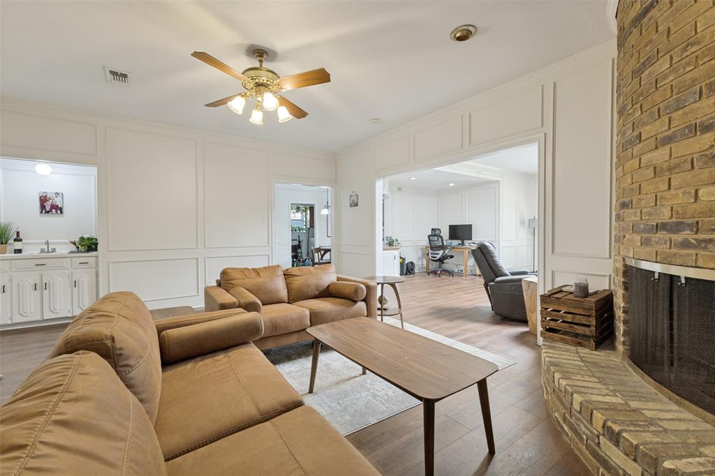 705 South Grove Road Richardson, TX 75081 - Photo 6 of 26 Living area featuring a brick fireplace with a metal screen, wood-finish flooring, and white paneled walls