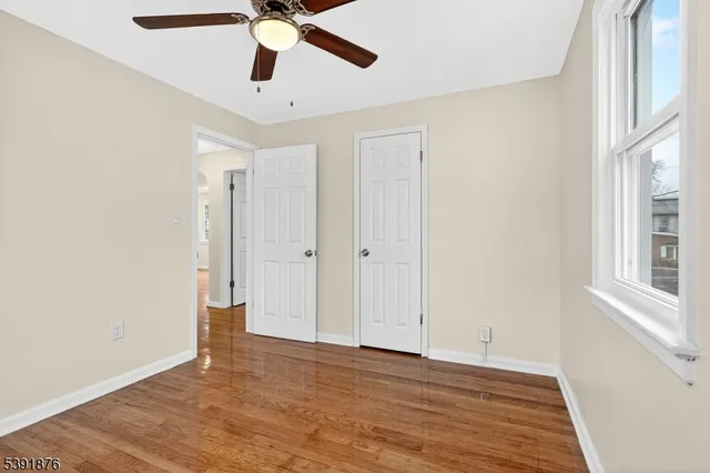 a view of an empty room with window a ceiling fan and wooden floor