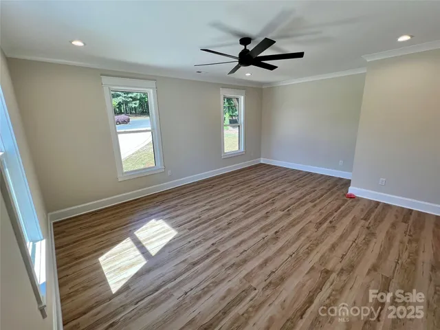 an empty room with wooden floor fan and windows