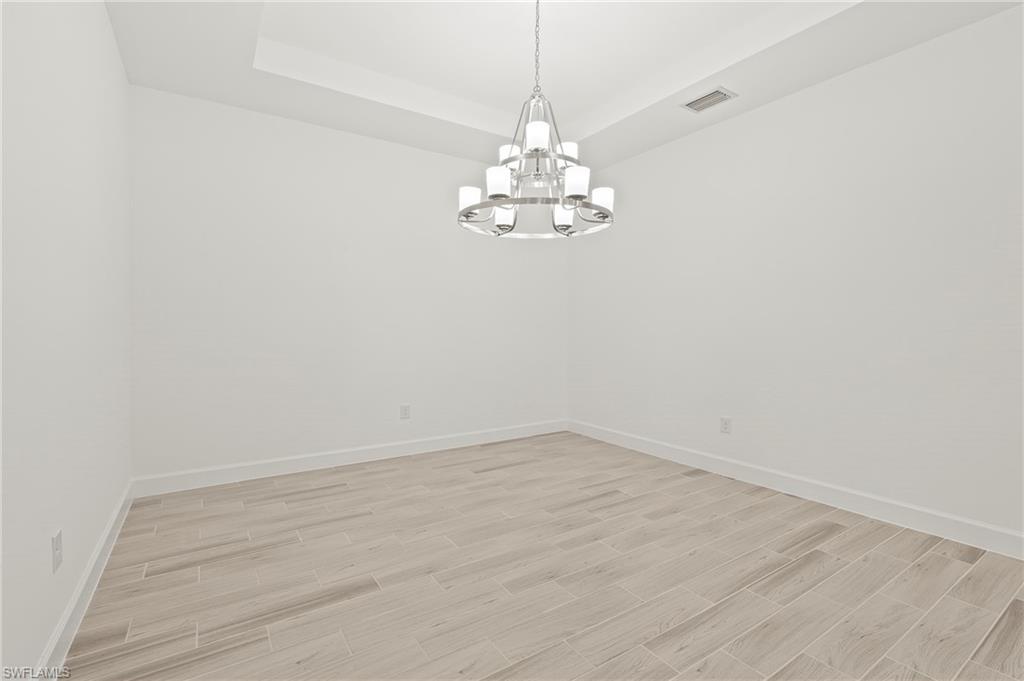 15517 Vittorio Street Naples, FL 34114 - Photo 8 of 35 Unfurnished room with a chandelier, light wood-type flooring, baseboards, and a raised ceiling