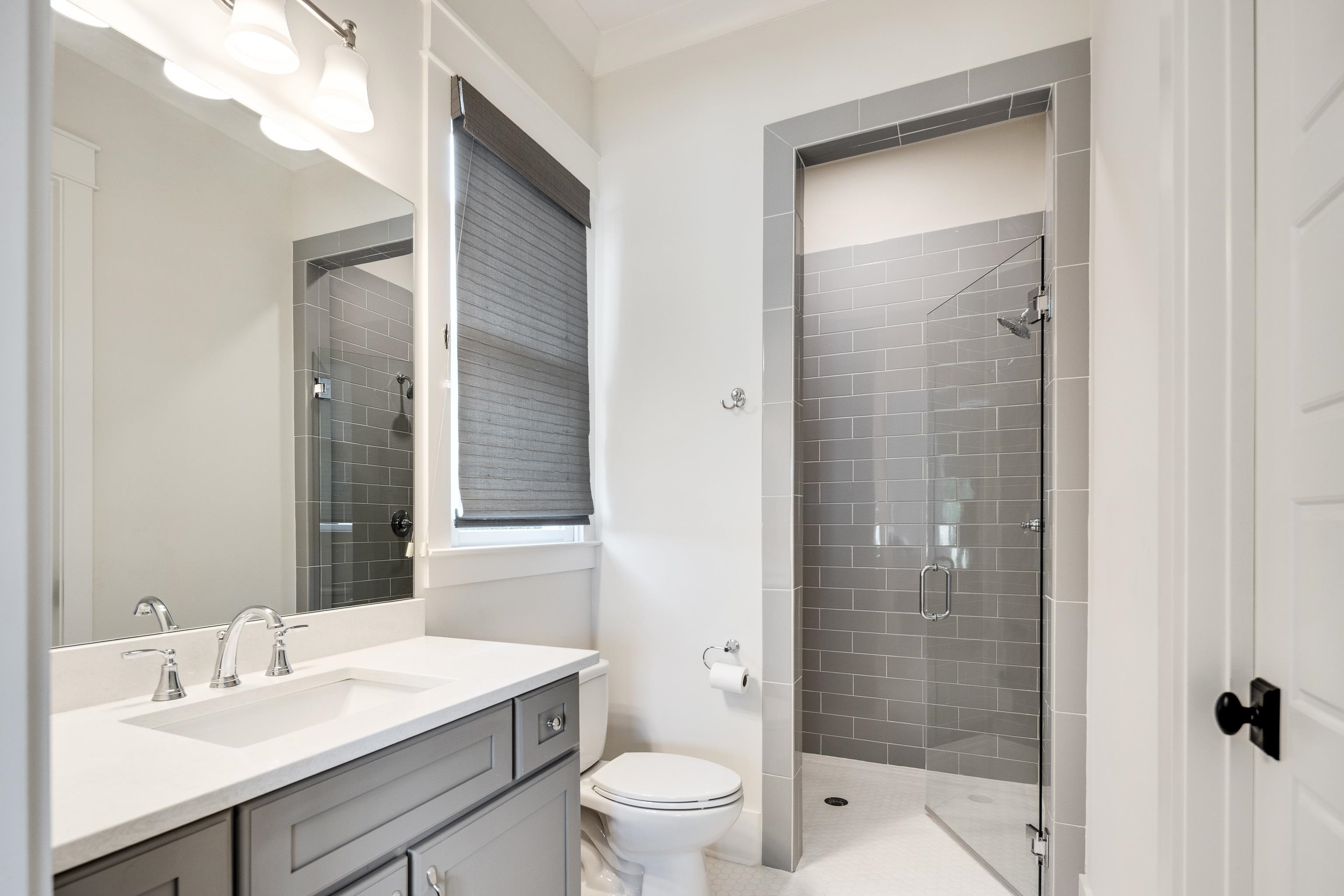100 Sunflower View Road Piperton, TN 38017 - Photo 24 of 29 Contemporary bathroom featuring a single vanity with a white countertop and gray cabinetry, an undermount sink with a polished chrome faucet, a frameless glass shower enclosure with gray subway tile, and a privacy window treatment
