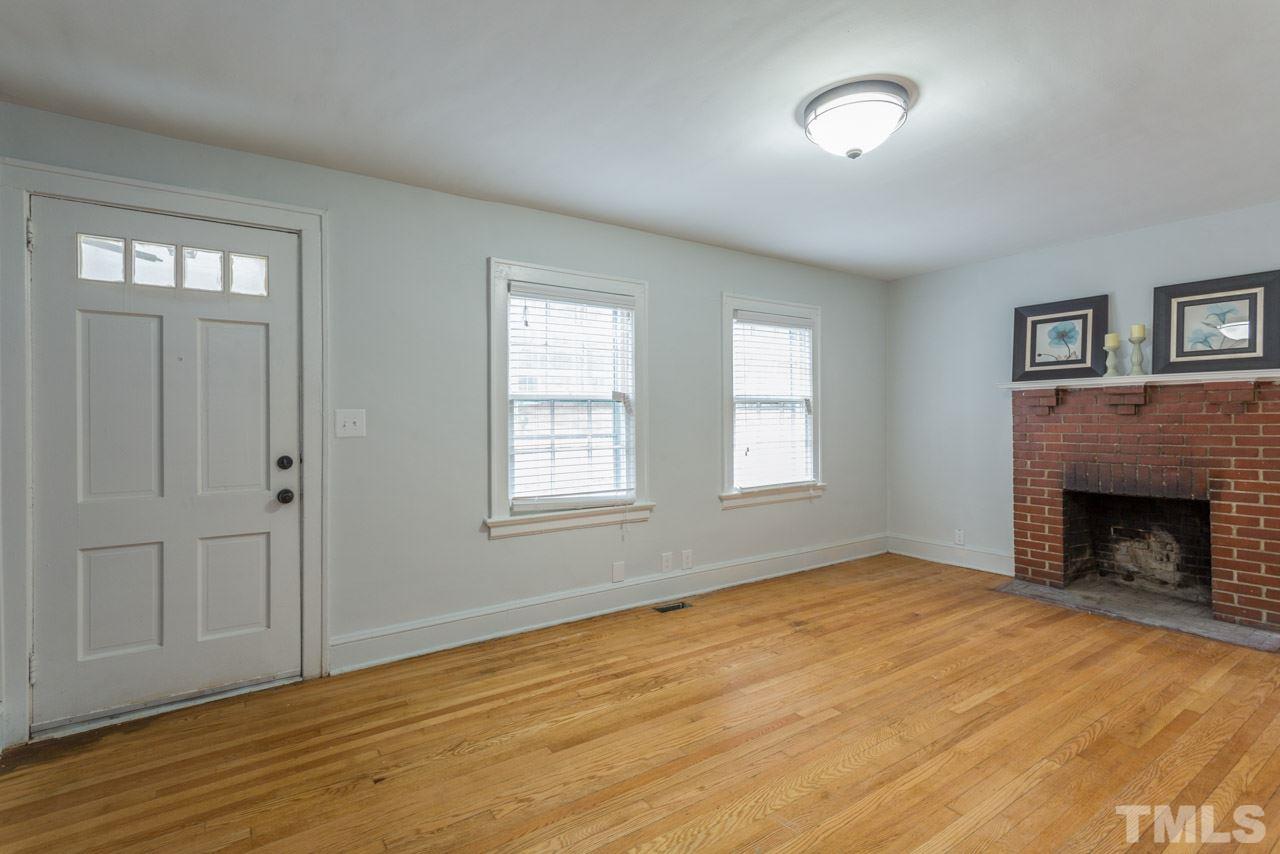 1215 Kent Road Raleigh, NC 27606 - Photo 2 of 11 an empty room with wooden floor fireplace and windows