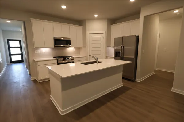 a kitchen with stainless steel appliances a stove a refrigerator a sink and white cabinets with wooden floor