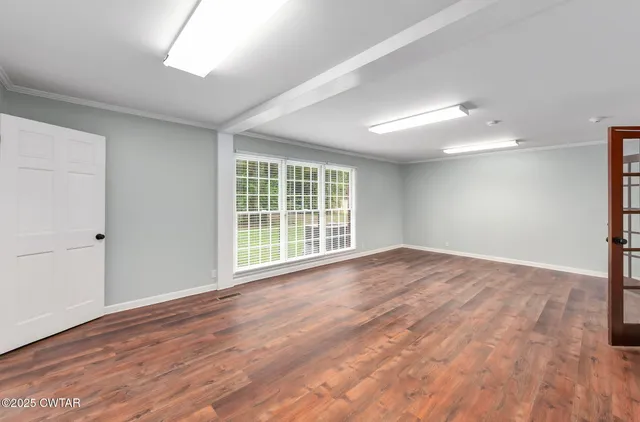 a view of an empty room with wooden floor and a window
