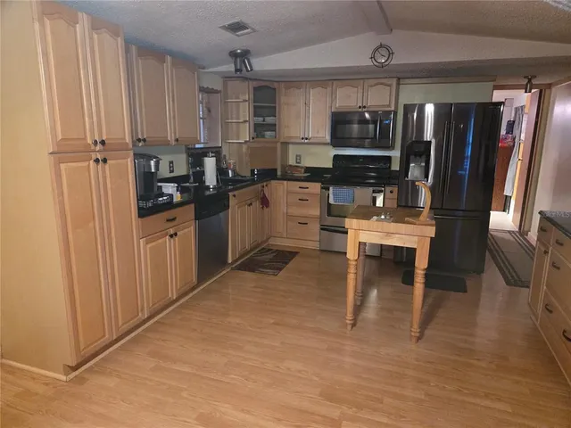 a kitchen with stainless steel appliances kitchen island granite countertop a refrigerator oven a sink dishwasher and white cabinets with wooden floor