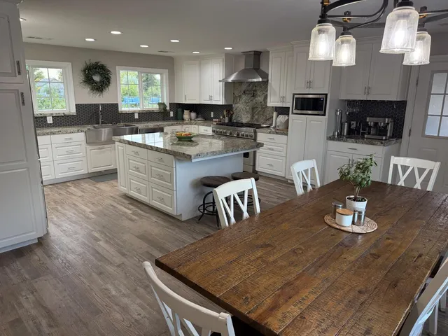 a kitchen with stainless steel appliances granite countertop a sink dishwasher a stove a dining table and chairs with wooden floor