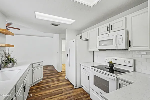 an empty room with wooden floor chandelier fan and windows
