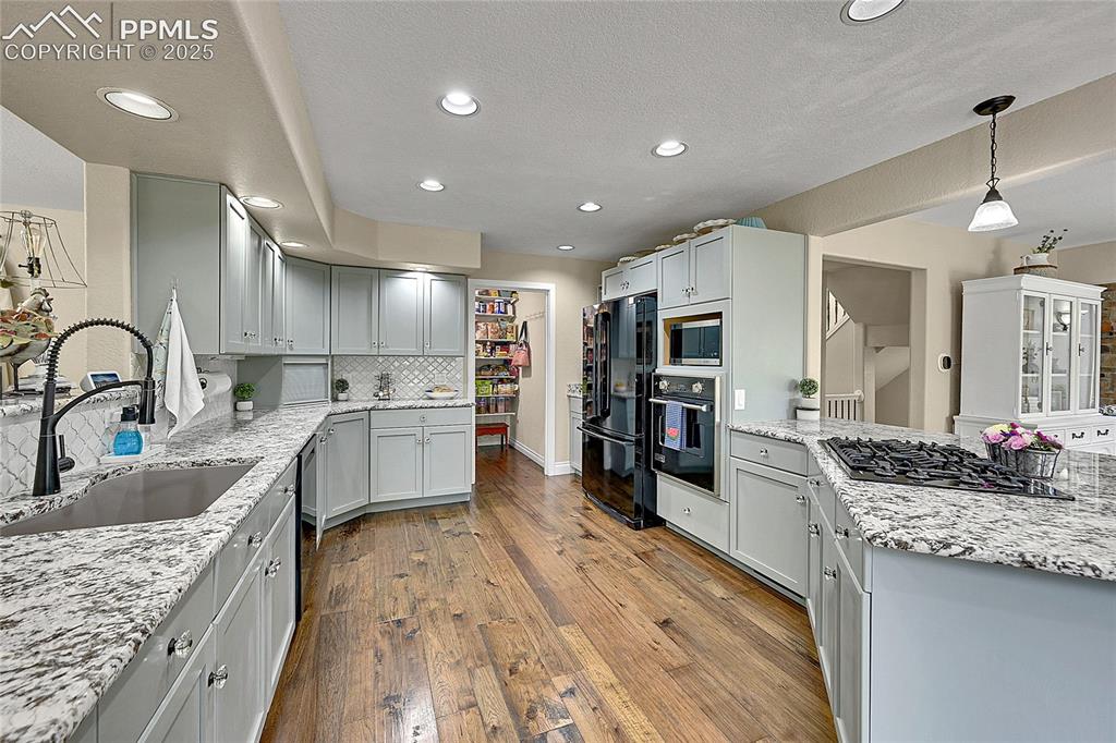 17350 Goshawk Road Colorado Springs, CO 80908 - Photo 13 of 50 a large kitchen with stainless steel appliances kitchen island granite countertop a large stove a sink dishwasher and white cabinets with wooden floor