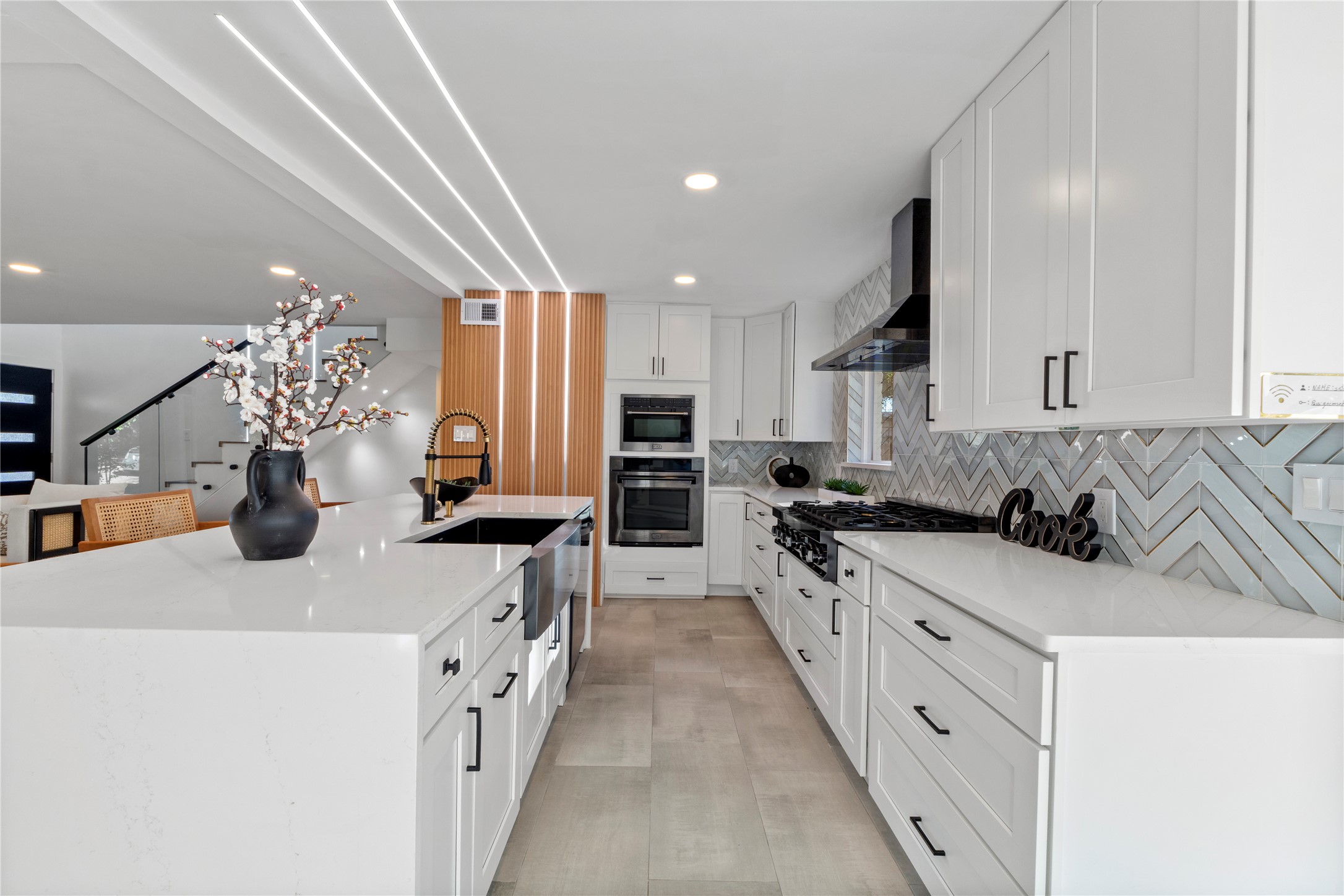 6604 Lexington Road Austin, TX 78757 - Photo 10 of 33 Kitchen with light stone countertops, a large island with sink, stainless steel oven, white cabinetry, and wall chimney range hood