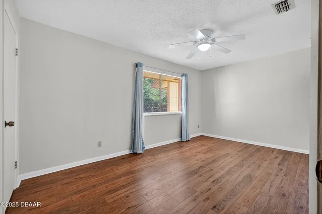 an empty room with wooden floor fan and windows