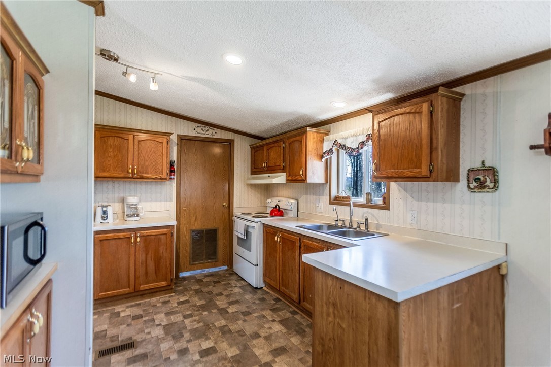 4502 Clover Road Cumberland, OH 43732 - Photo 12 of 38 Kitchen with wood finish cabinets, white range with electric cooktop, light countertops, ornamental molding, and stainless steel microwave