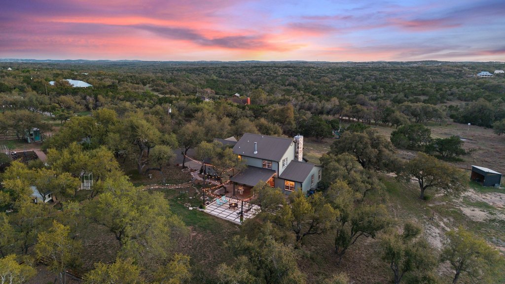 An aerial panorama reveals a private home nestled amidst a dense, verdant landscape at sunset.