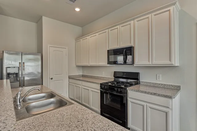 a kitchen with granite countertop a sink a stove top oven and white cabinets