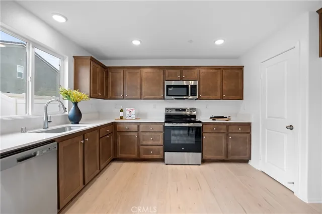 a kitchen with stainless steel appliances granite countertop a stove top oven a sink dishwasher and a refrigerator with wooden cabinets