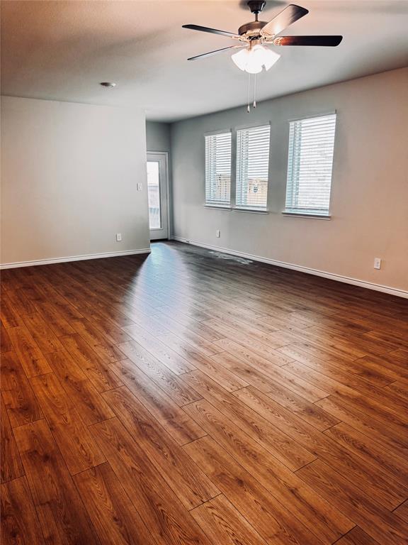 2625 Lewisville Road Celina, TX 75009 - Photo 3 of 7 Spacious living room featuring wood-finish flooring, a ceiling fan with integrated lighting, multiple windows with blinds, and a glass-paneled door