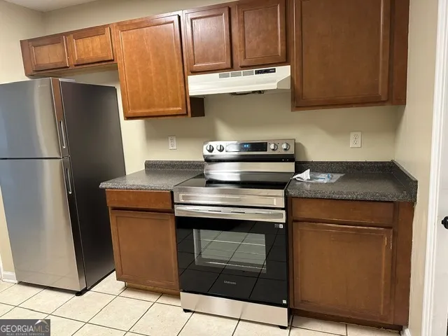 a view of a refrigerator in kitchen and an empty room in wooden floor