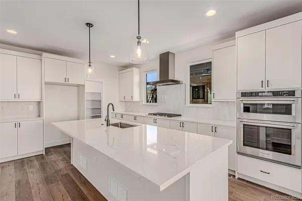 a large white kitchen with a stove a sink a refrigerator and a wooden floor