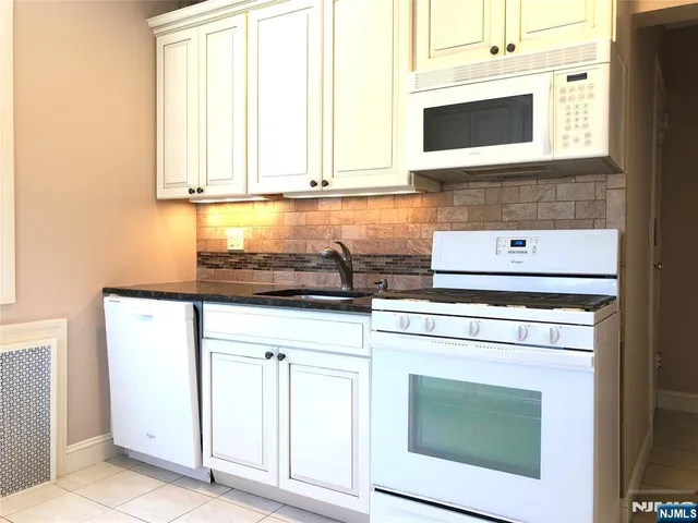 a kitchen with stainless steel appliances granite countertop white cabinets sink and window