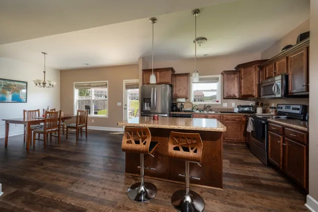 a kitchen with stainless steel appliances granite countertop a stove top oven a refrigerator a dining table and chairs with wooden floor