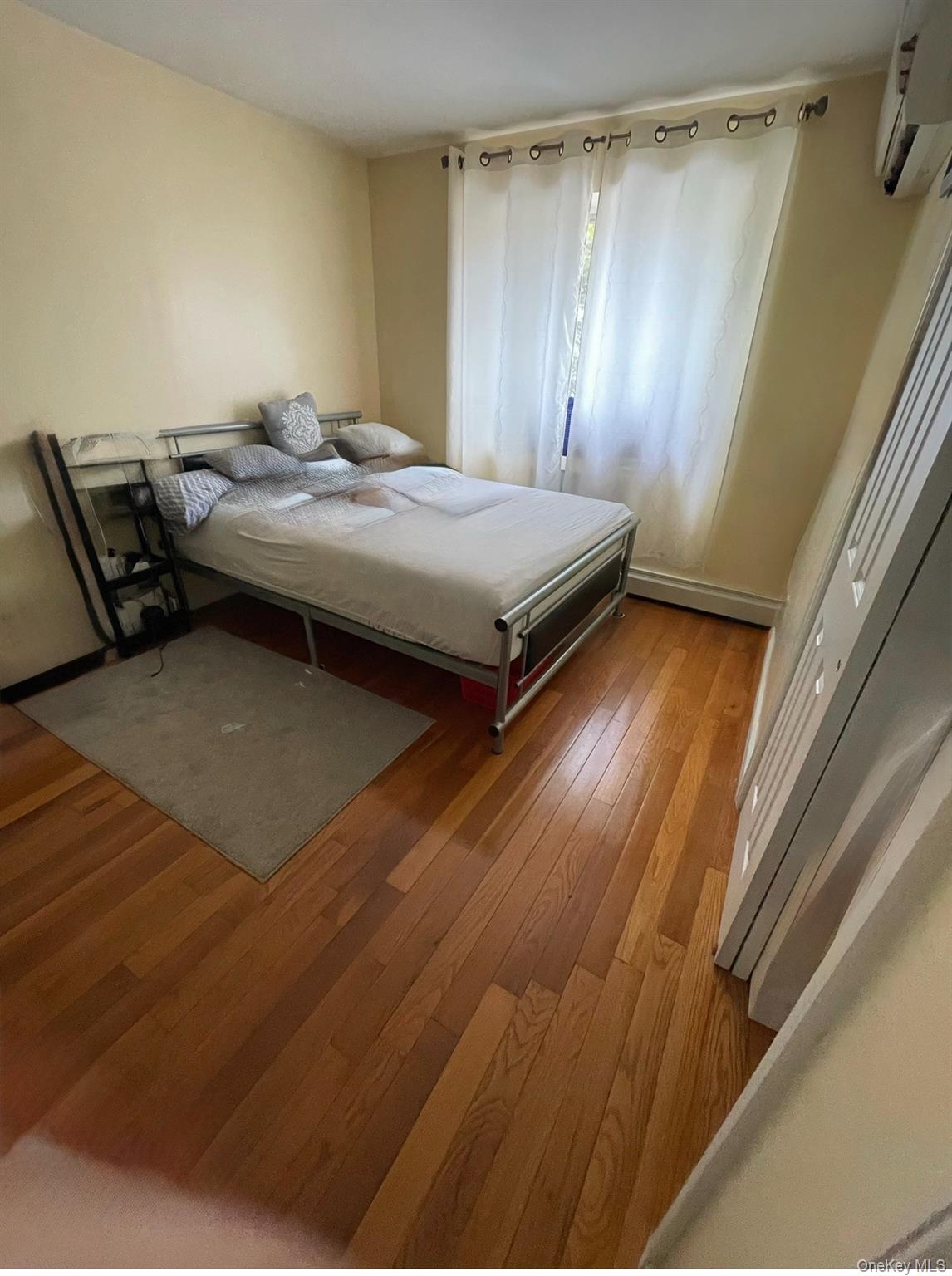 137-08 31st Road, Unit 5D Queens, NY 11354 - Photo 3 of 4 Bedroom featuring light wood-type flooring, a wall mounted AC, and a baseboard heating unit