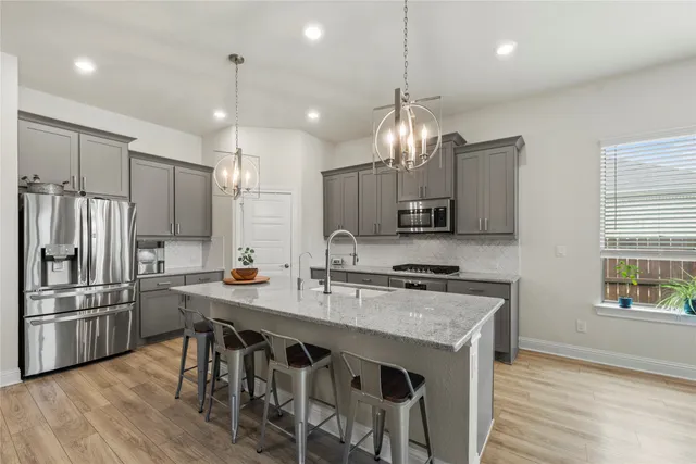 a kitchen with stainless steel appliances granite countertop a sink a stove a refrigerator cabinets and chairs