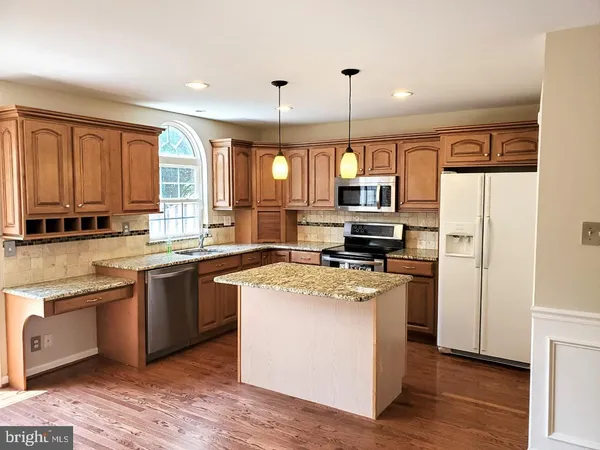 a kitchen with stainless steel appliances granite countertop a stove a sink dishwasher a refrigerator and white cabinets with wooden floor