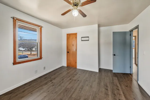 a view of an empty room with wooden floor and a ceiling fan