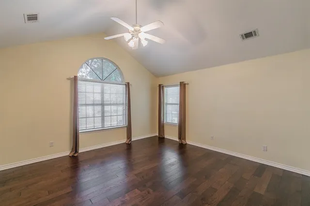 an empty room with wooden floor chandelier fan and windows