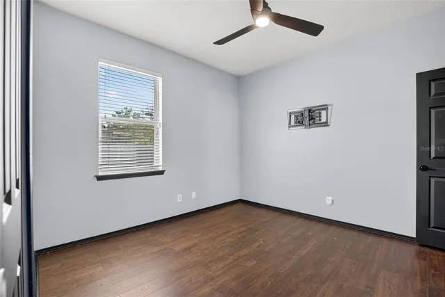 an empty room with wooden floor chandelier fan and windows