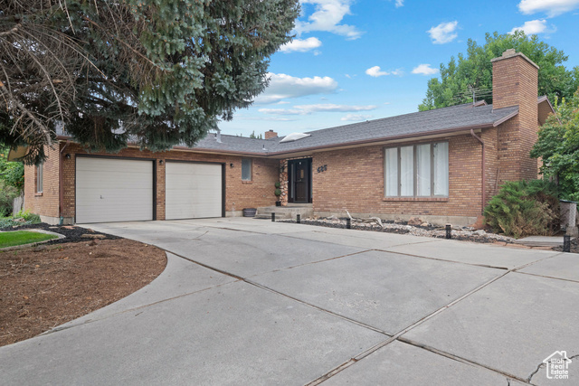 Ranch-style house featuring a chimney, concrete driveway, brick siding, and a shingled roof