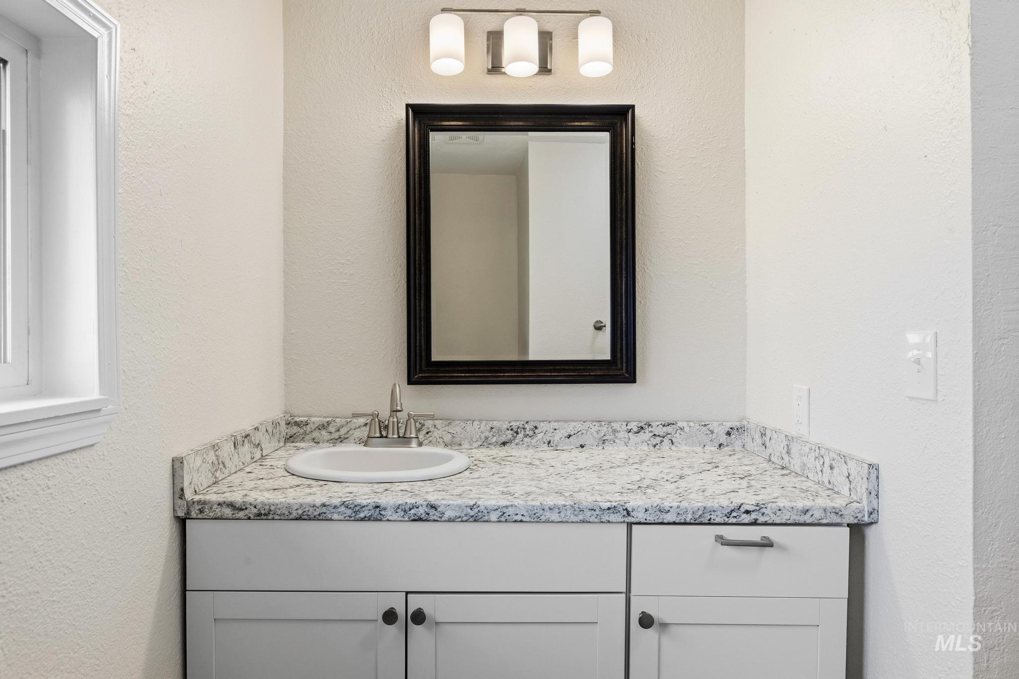 14666 Willis Road Caldwell, ID 83607 - Photo 30 of 50 Bathroom vanity featuring a white cabinet, speckled countertop, and integrated sink with a brushed nickel faucet