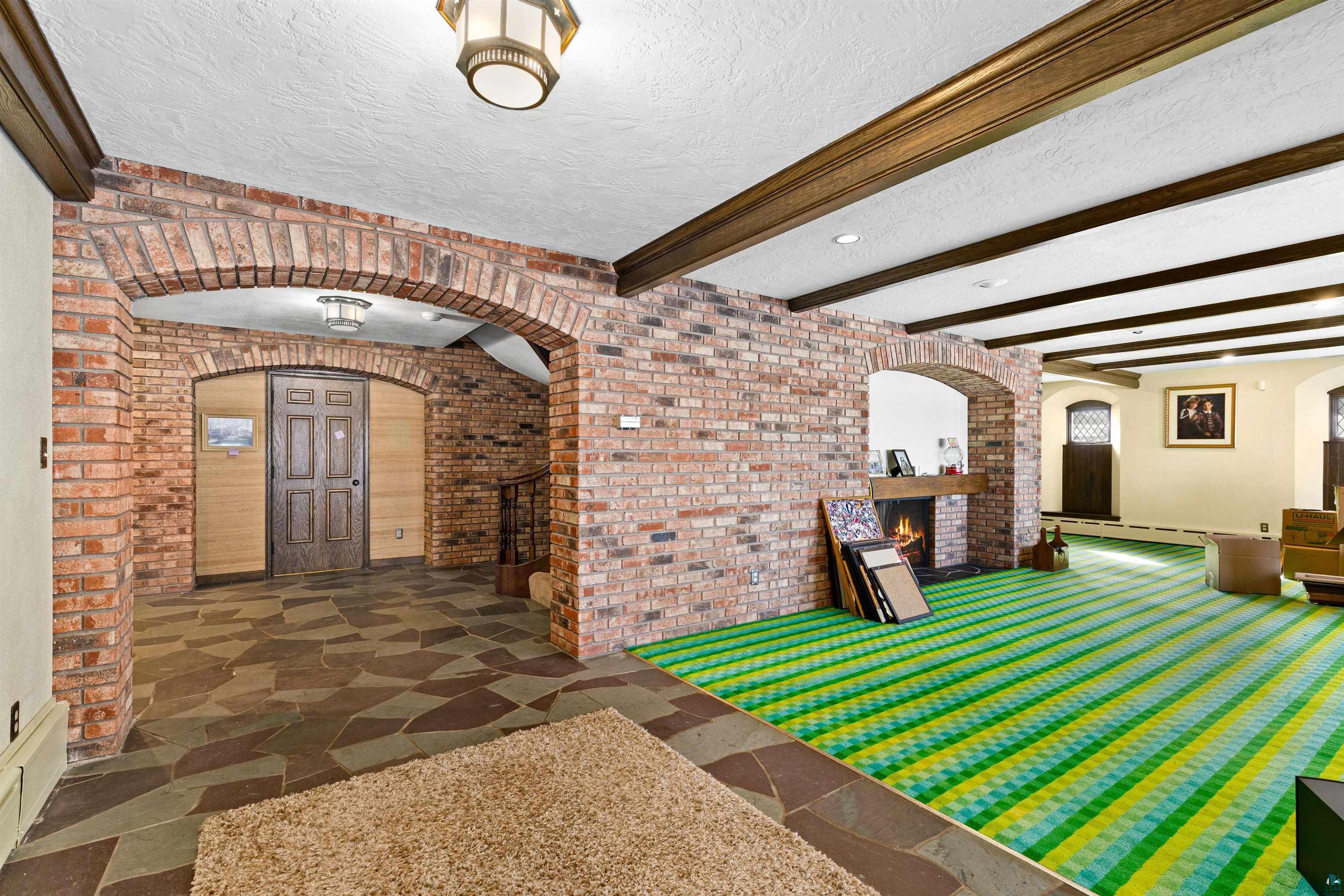 5781 South Pike Lake Road Duluth, MN 55811 - Photo 37 of 42 Playroom with arched walkways, brick wall, a textured ceiling, a fireplace, and beam ceiling