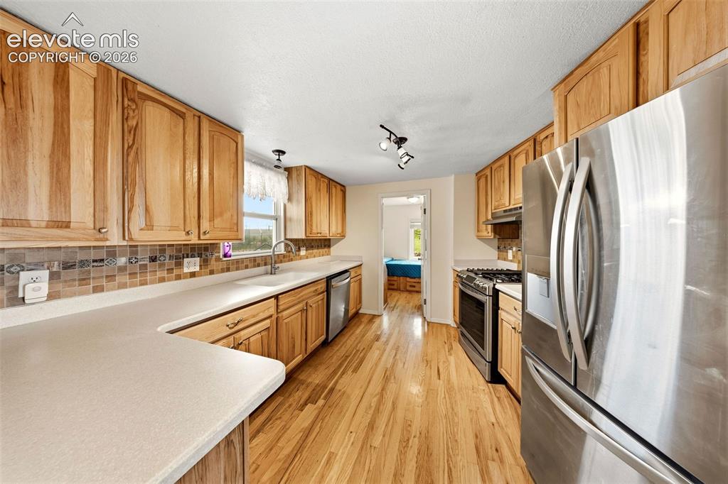 13075 Blaney Road South Peyton, CO 80831 - Photo 8 of 40 U-shaped kitchen featuring light wood cabinetry, light-toned countertops, a mosaic tile backsplash, and stainless steel appliances