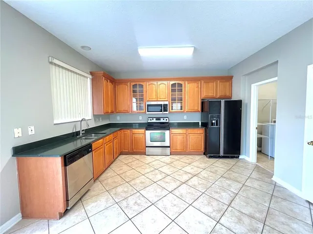 a large kitchen with granite countertop a stove a sink a refrigerator a window and red cabinets