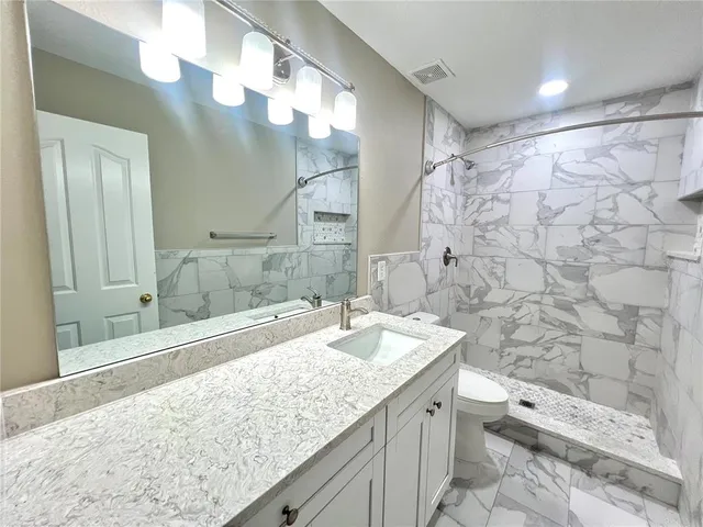 a bathroom with a granite countertop sink a toilet and shower