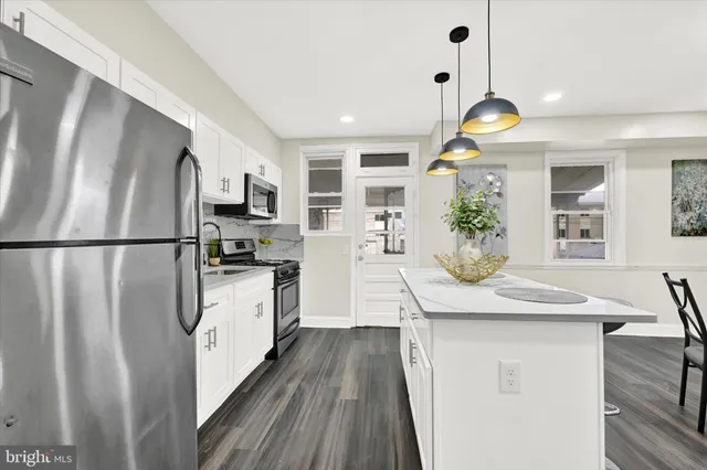 a kitchen with stainless steel appliances granite countertop a refrigerator a sink dishwasher a stove and a dining table with wooden floor