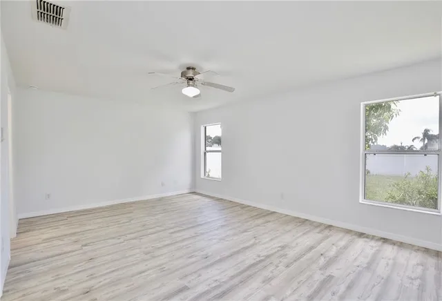 an empty room with wooden floor fan and windows