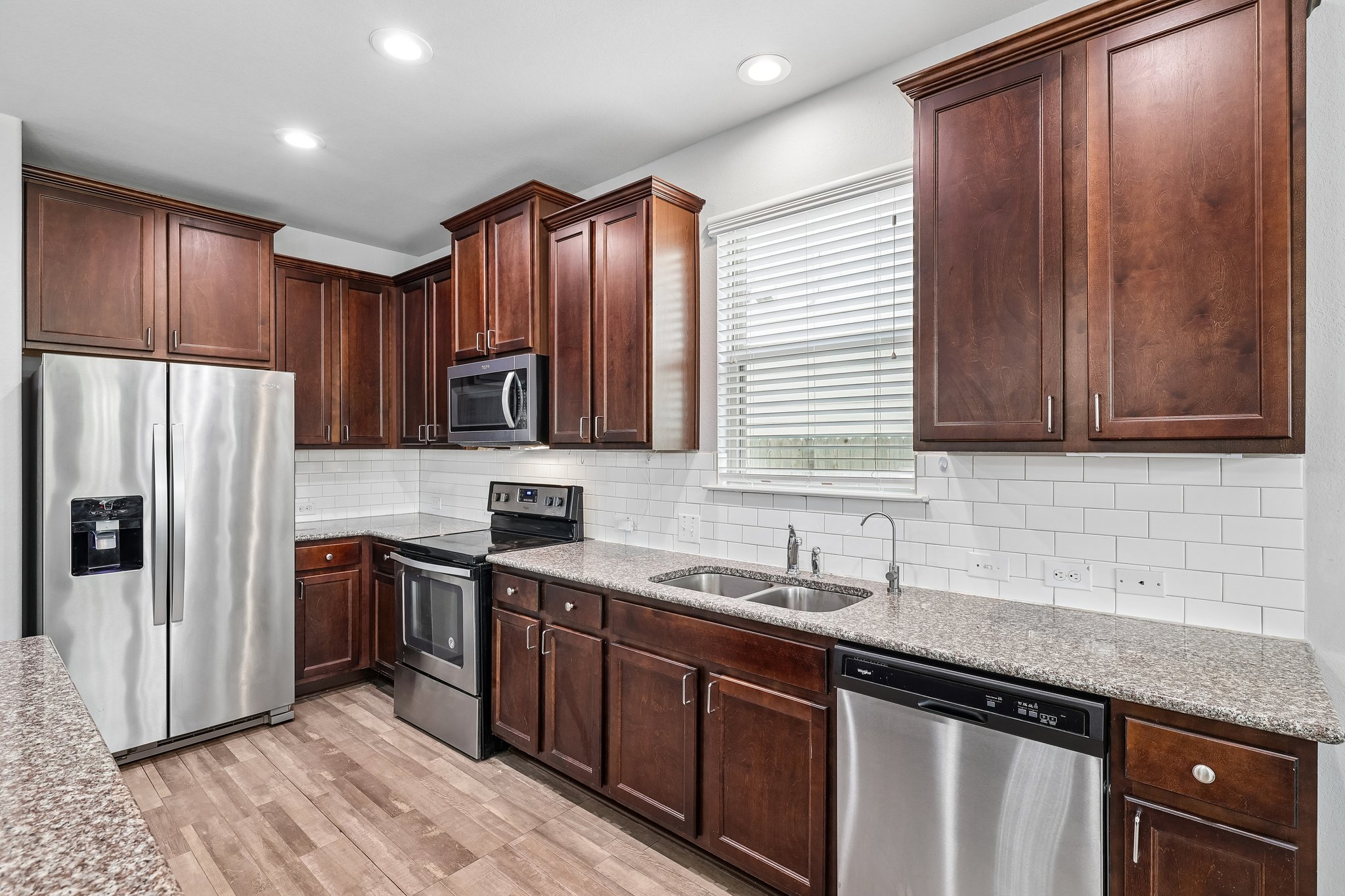 387 Guemal Road Buda, TX 78610 - Photo 13 of 39 Kitchen featuring dark wood cabinetry, stainless steel appliances, speckled stone countertops, a white subway tile backsplash, and wood-finish flooring