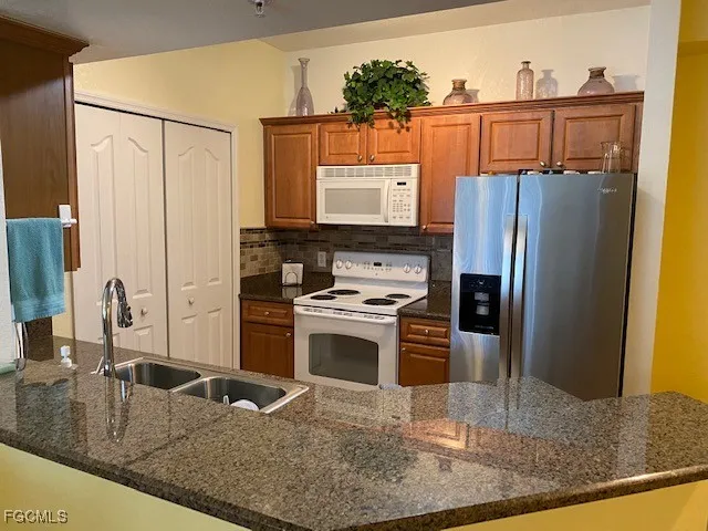 a kitchen with stainless steel appliances granite countertop a refrigerator a stove and a sink with wooden cabinets