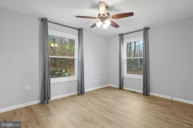 an empty room with wooden floor fan and windows