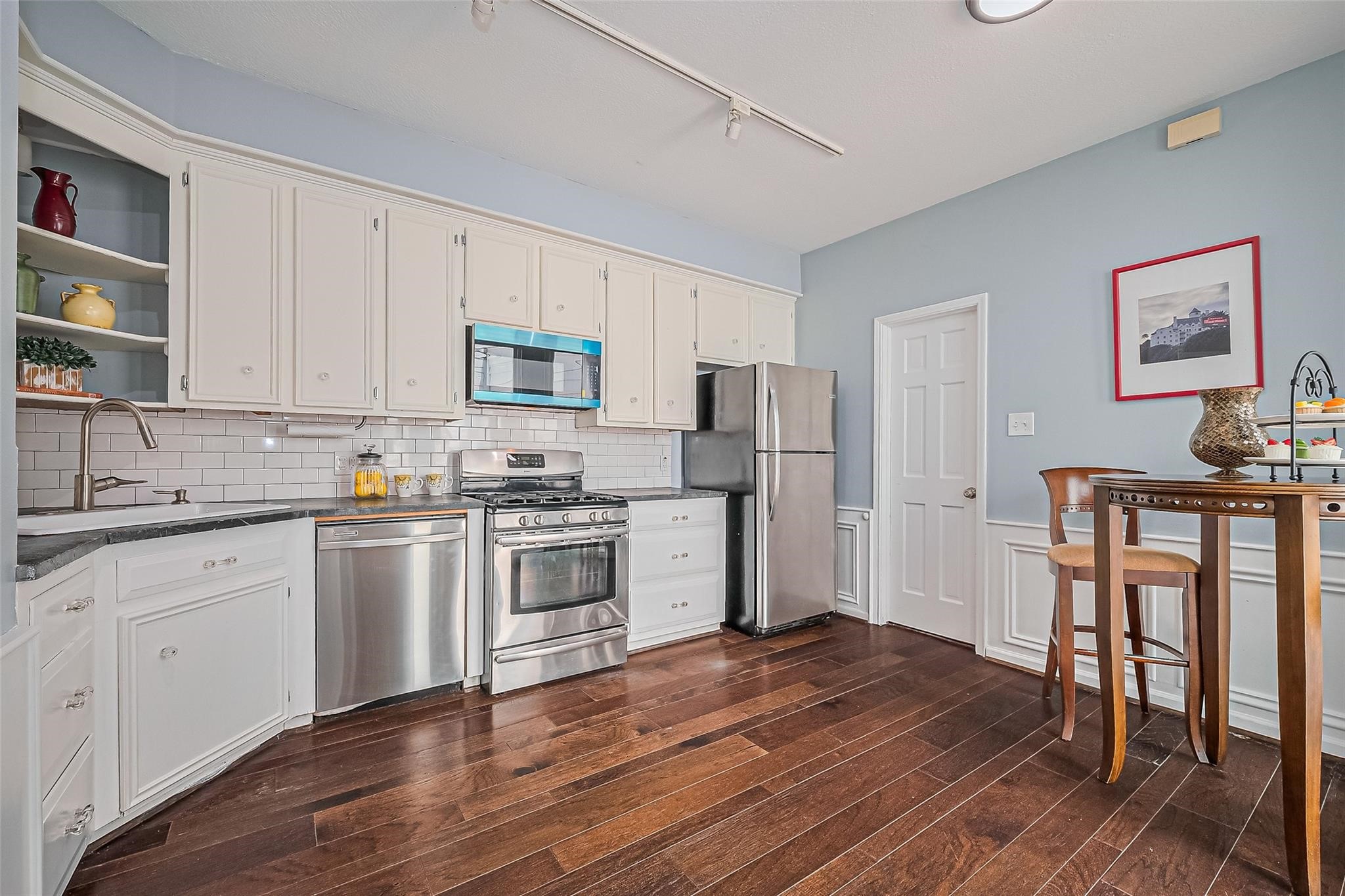 4305 Westheimer Road Houston, TX 77027 - Photo 6 of 25 Charming kitchen with sleek stainless steel appliances, classic white cabinetry, and rich hardwood flooring, perfect for modern living.