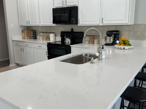a kitchen with stainless steel appliances a sink a stove a microwave a sink a refrigerator white cabinets and black granite counter tops