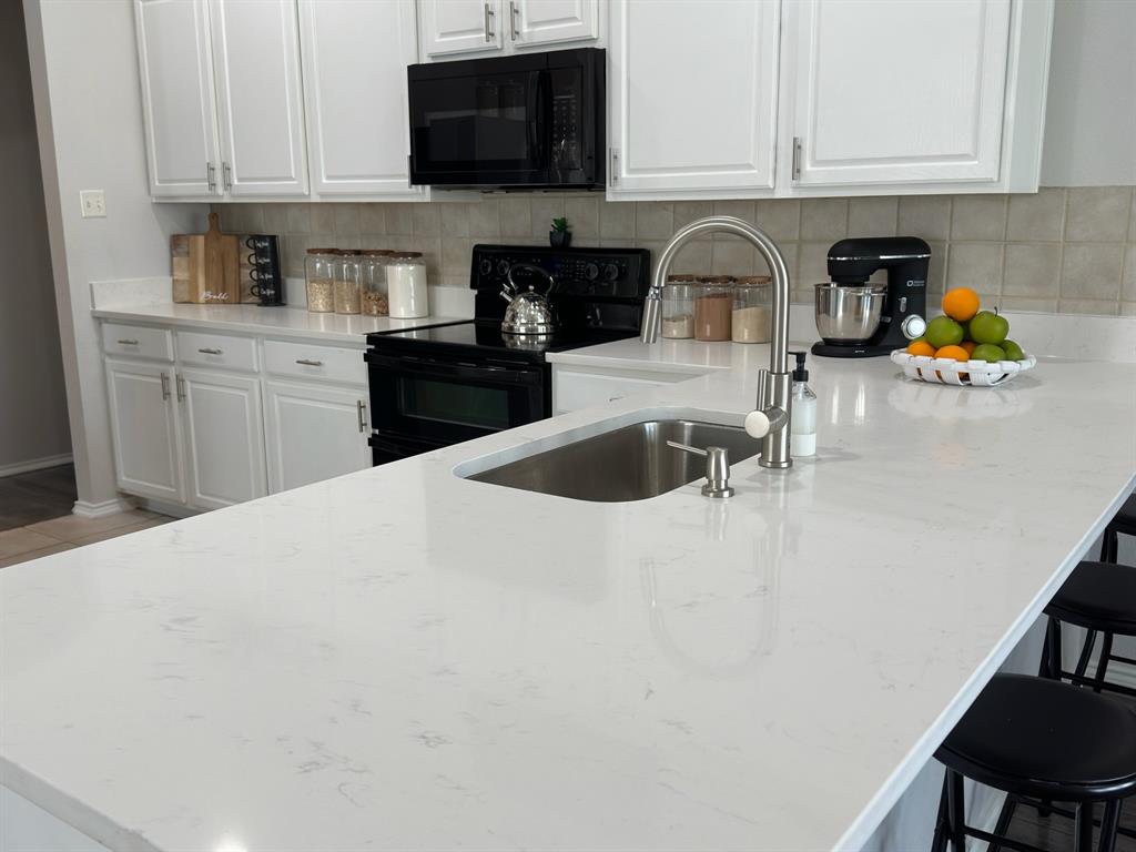 213 Arabian Road Waxahachie, TX 75165 - Photo 4 of 29 Kitchen featuring white cabinets, black appliances, and light stone countertops