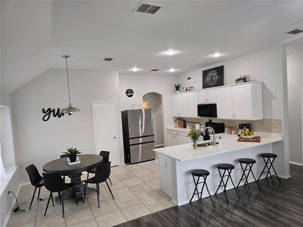 213 Arabian Road Waxahachie, TX 75165 - Photo 6 of 29 Kitchen with a peninsula, freestanding refrigerator, a kitchen bar, white cabinets, and arched walkways
